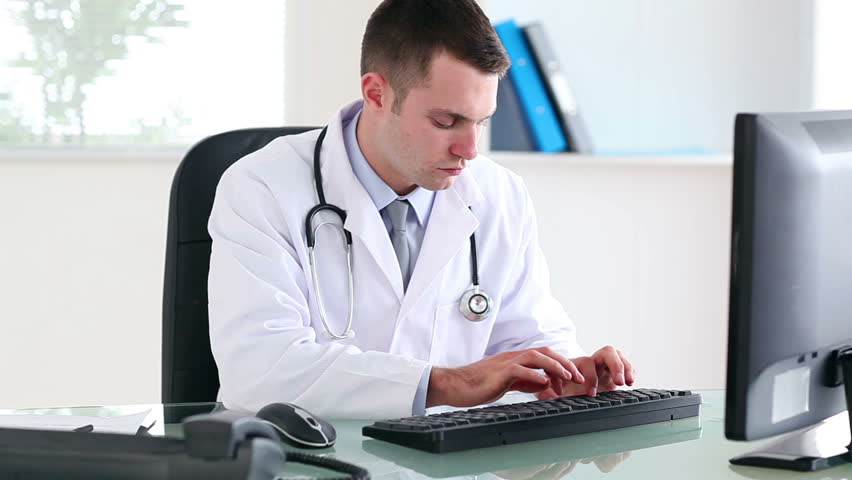 Doctor Working On Computer Smiling Doctor Working In Office On His Computer Stock
